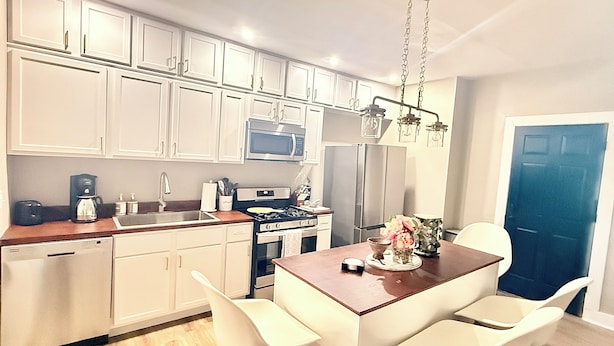 A modern kitchen with white cabinets, a gas stove, a microwave, and a refrigerator. There is a dining table with white chairs and a vase of flowers. - Spacious Family Fun Retreat 3 min to Beach/Zoo/Outlet Fenced Backyard w/ Deck (Michigan City)