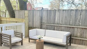 A wooden deck with a white sofa and two wooden chairs. - Spacious Family Fun Retreat 3 min to Beach/Zoo/Outlet Fenced Backyard w/ Deck (Michigan City)
