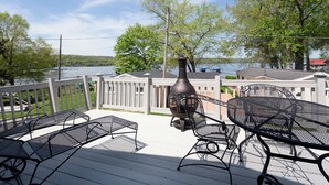 A deck with outdoor furniture, a grill, and a view of a lake and buildings. - Charming 3-bedroom house in Conesus with lake access and dock for boat (Conesus)