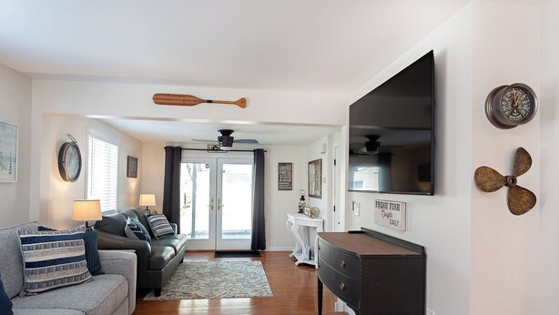 A living room with a sofa, a coffee table, a TV mounted on the wall, and a ceiling fan. - Charming 3-bedroom house in Conesus with lake access and dock for boat (Conesus)