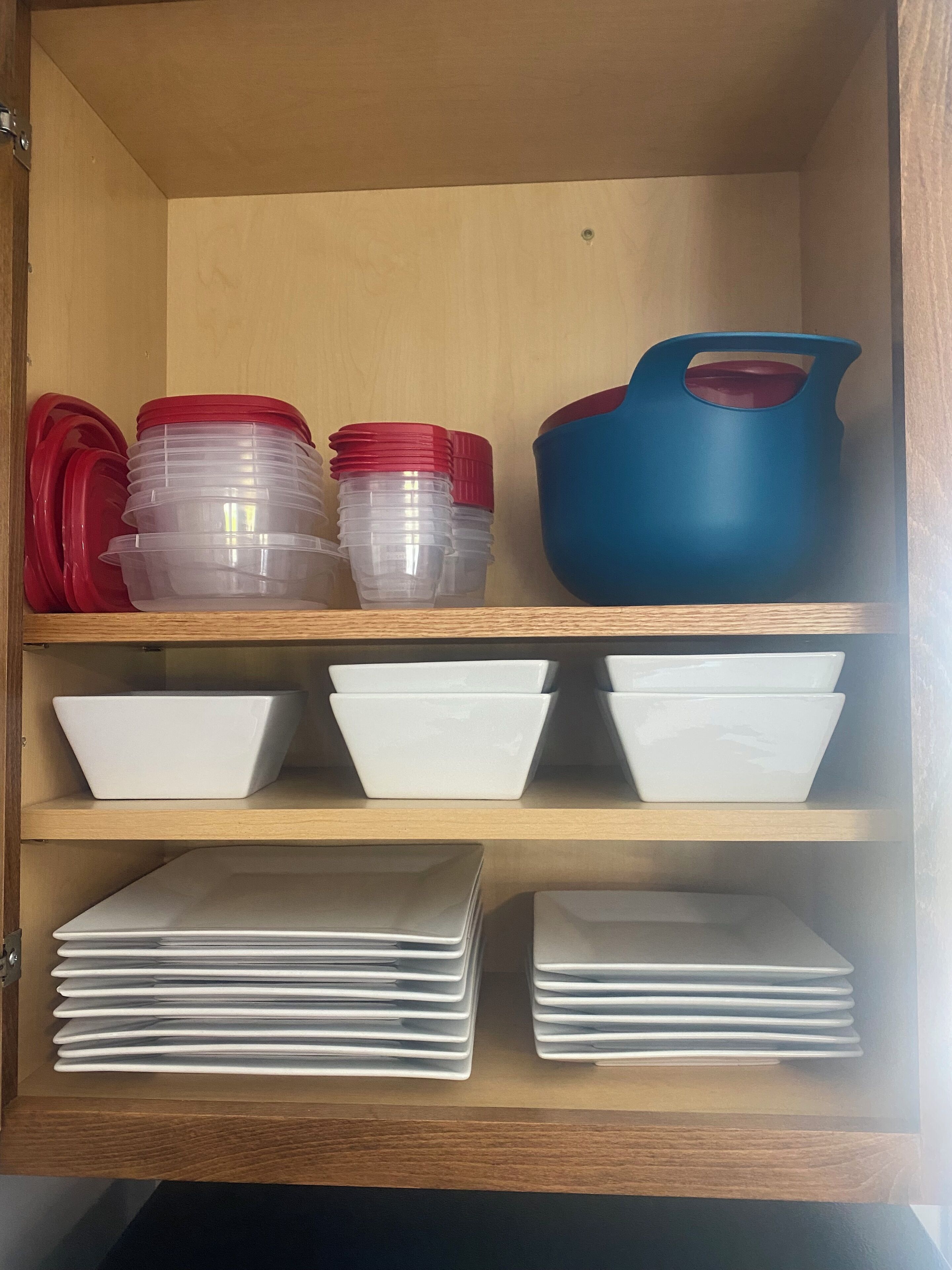 Un meuble en bois contenant des récipients en plastique transparent avec des couvercles rouges, des bols blancs et un pichet bleu.