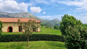 A building with a red-tiled roof, surrounded by lush green fields and mountains in the background.