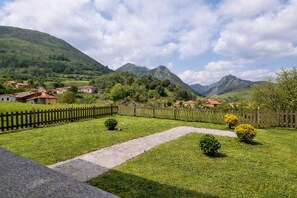 Paisagem rural com um caminho pavimentado, cerca de madeira e casas ao fundo.