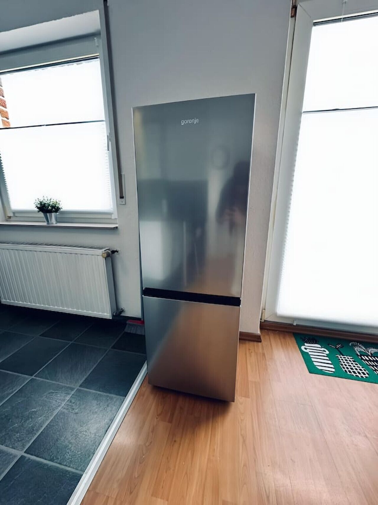 Uma cozinha moderna com frigorífico de aço inoxidável, uma janela com persianas e um radiador.