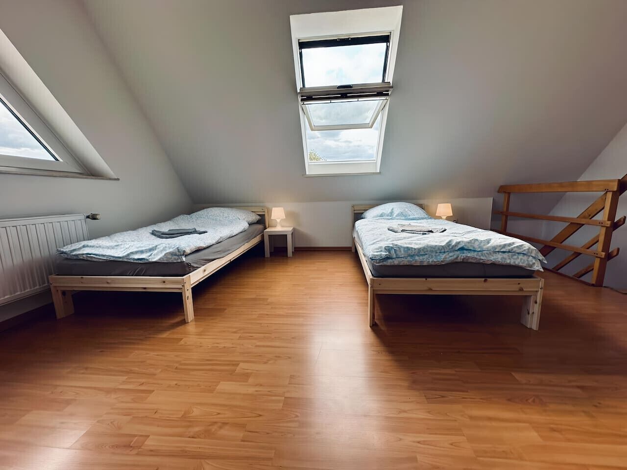 A room with two wooden beds, a skylight, and a wooden ladder.