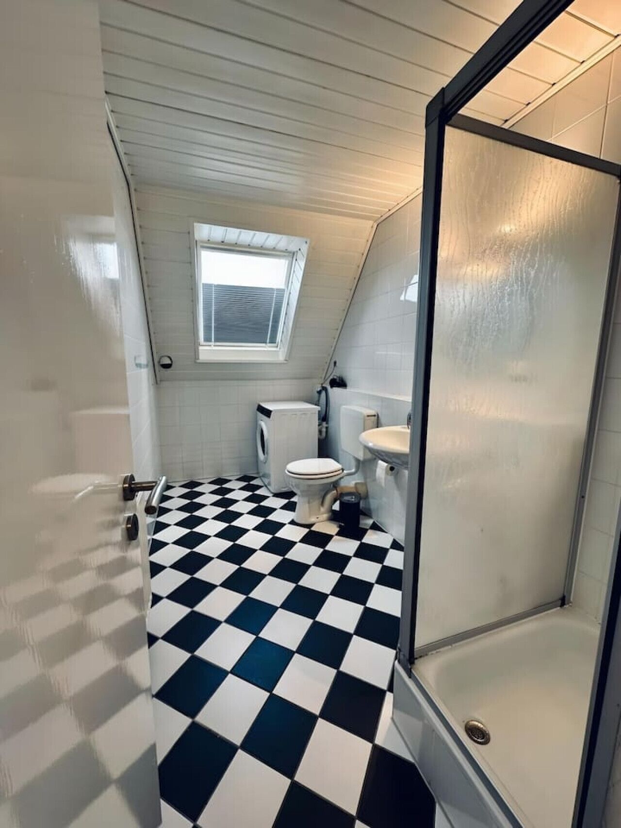 Une petite salle de bain aux dimensions réduites, avec un carrelage noir et blanc à motifs géométriques, des toilettes, un lavabo et un espace douche.