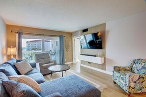 Una sala de estar con sofá, sillón, mesa de centro, televisor y una silla estampada.