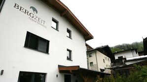 A white building with 'BERGZEIT Appartments' signage, multiple windows, and a stone wall with potted plants. - Hohe Salve by Interhome (Wildschönau)