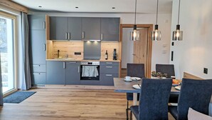 A modern kitchen with grey cabinets, a wooden countertop, and a built-in oven. There is a dining area with a table and chairs, and a large window providing natural light. - Hohe Salve by Interhome (Wildschönau)