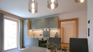 A modern kitchen with grey cabinets, a built-in oven, and a dining area with a table and chairs. - Hohe Salve by Interhome (Wildschönau)