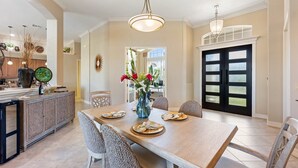 A spacious dining area with a wooden table and chairs, a vase with flowers, and a kitchen in the background.
