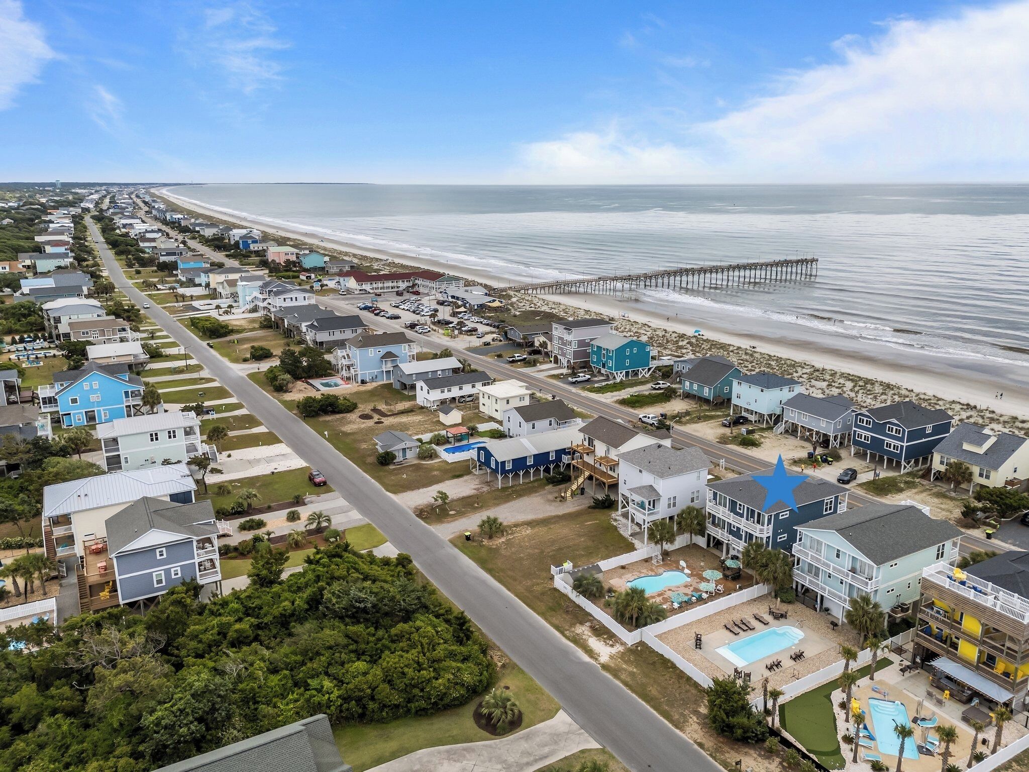 An aerial view of a coastal residential area with houses, a beach, and a pier.
