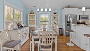 A dining area with a table set for four, surrounded by white cabinetry and a kitchen area with a refrigerator, microwave, and bar stools. - Discover Peaceful Palms, a charming 3-bedroom home in Oak Island's East Beach (Oak Island)