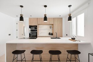 A modern kitchen with a large island, black bar stools, and pendant lighting.