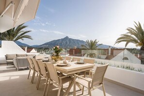 A rooftop terrace with a dining table set for six, surrounded by chairs, overlooking a mountain range. - 5 BR Luxury apt w Pool,  garage and amazing views (Marbella)