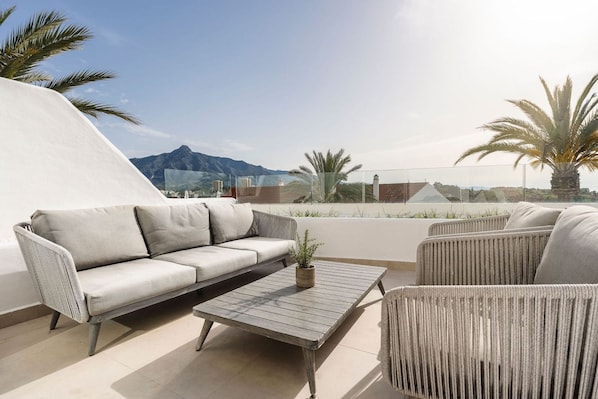 A rooftop terrace with a sofa, chairs, and a table.