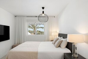 A hotel room with a bed, a TV, a lamp, and a window with curtains.