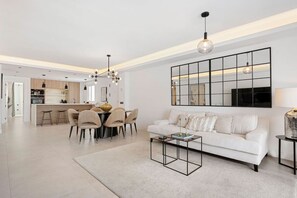 A modern living room with a white sofa, a dining table with chairs, and a kitchen in the background. - 5 BR Luxury apt w Pool,  garage and amazing views (Marbella)