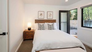 A bedroom with a bed, a nightstand with a lamp, two framed pictures on the wall, and a sliding glass door leading to an outdoor area.