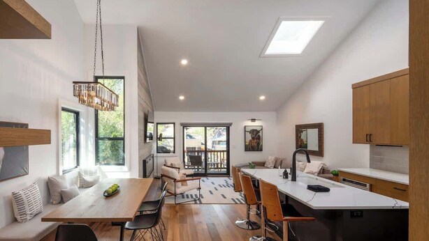 A modern kitchen with a dining area, wooden cabinets, and a large window.