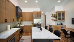 A modern kitchen with wooden cabinets, a central island, a built-in oven, and a stainless steel refrigerator.
