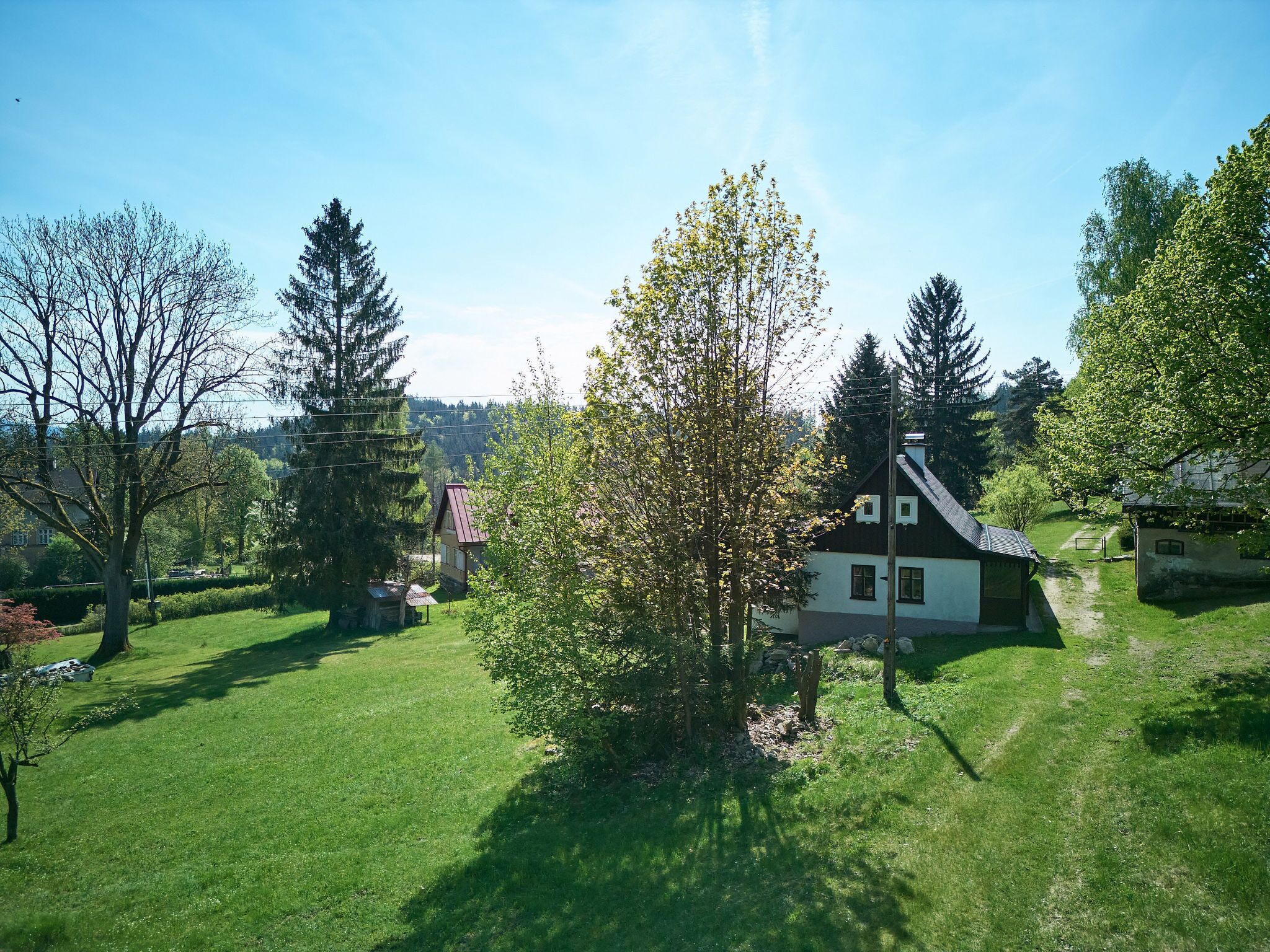 Une maison de campagne avec un toit en pente, entourée d’une pelouse bien entretenue et d’arbres.