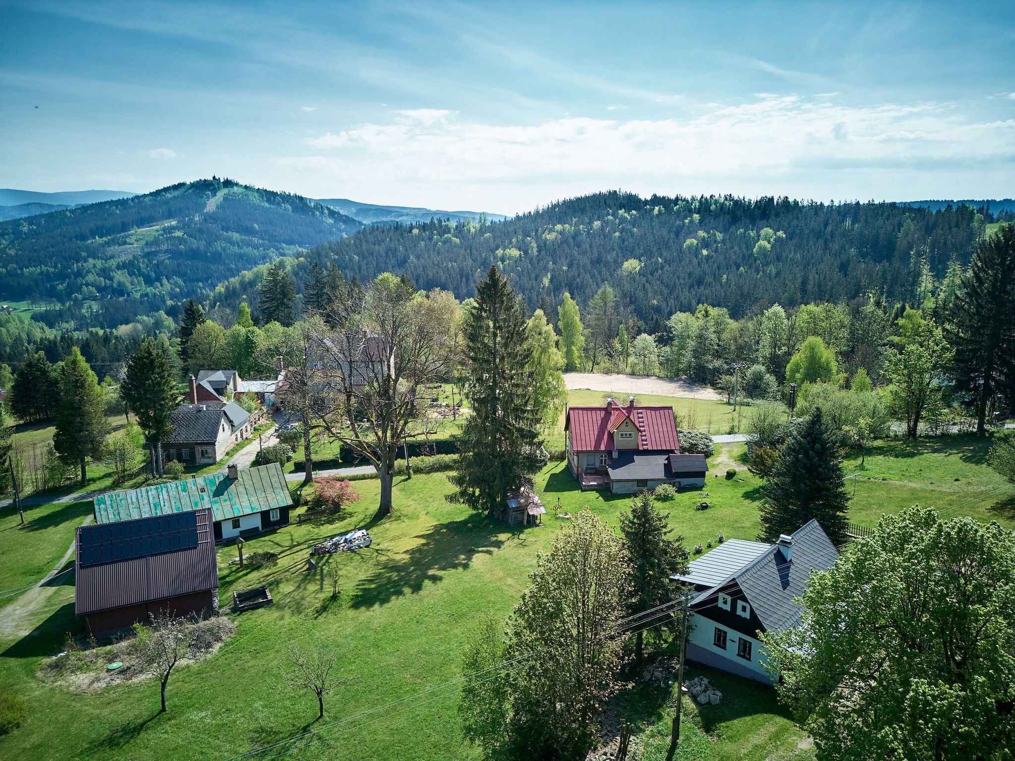 Ländliche Landschaft mit Häusern, grünen Feldern und bewaldeten Hügeln.