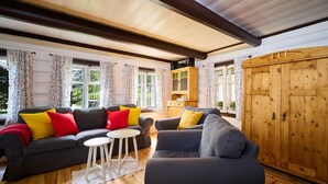 A cozy living room with a dark grey sofa, a smaller grey armchair, and a wooden cabinet. There are two white round tables and a small white rug on the wooden floor. - Vacation home Marta by Interhome (Smržovka)