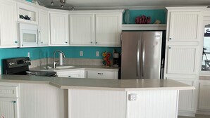 A modern kitchen with white cabinetry, a stainless steel refrigerator, and a teal accent wall. - Tides & Tranquility - Venture Out Unit 053 (Summerland Key)