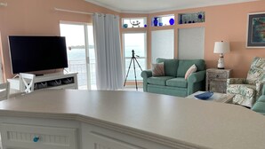 A living room with a TV, green sofa, and a view of the sea. - Tides & Tranquility - Venture Out Unit 053 (Summerland Key)