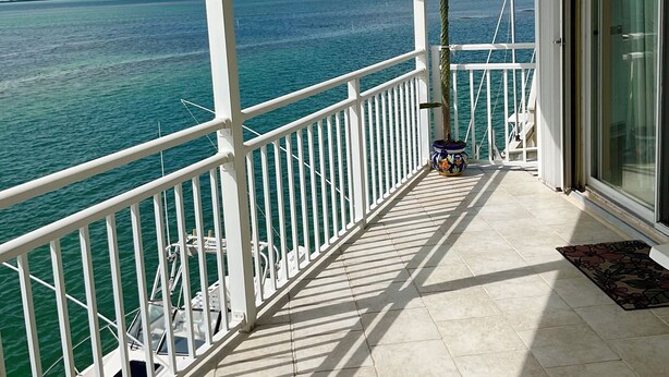 A balcony with a view of the ocean, a white railing, and a door leading to a room. - Tides & Tranquility - Venture Out Unit 053 (Summerland Key)