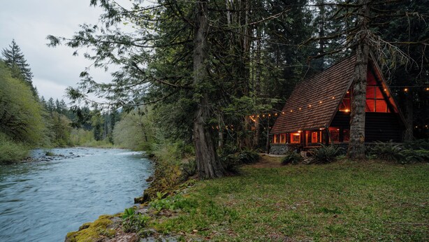 Una cabaña junto a un río, rodeada de árboles.