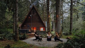 Una cabaña en un bosque con un camino de grava, rodeada de árboles.