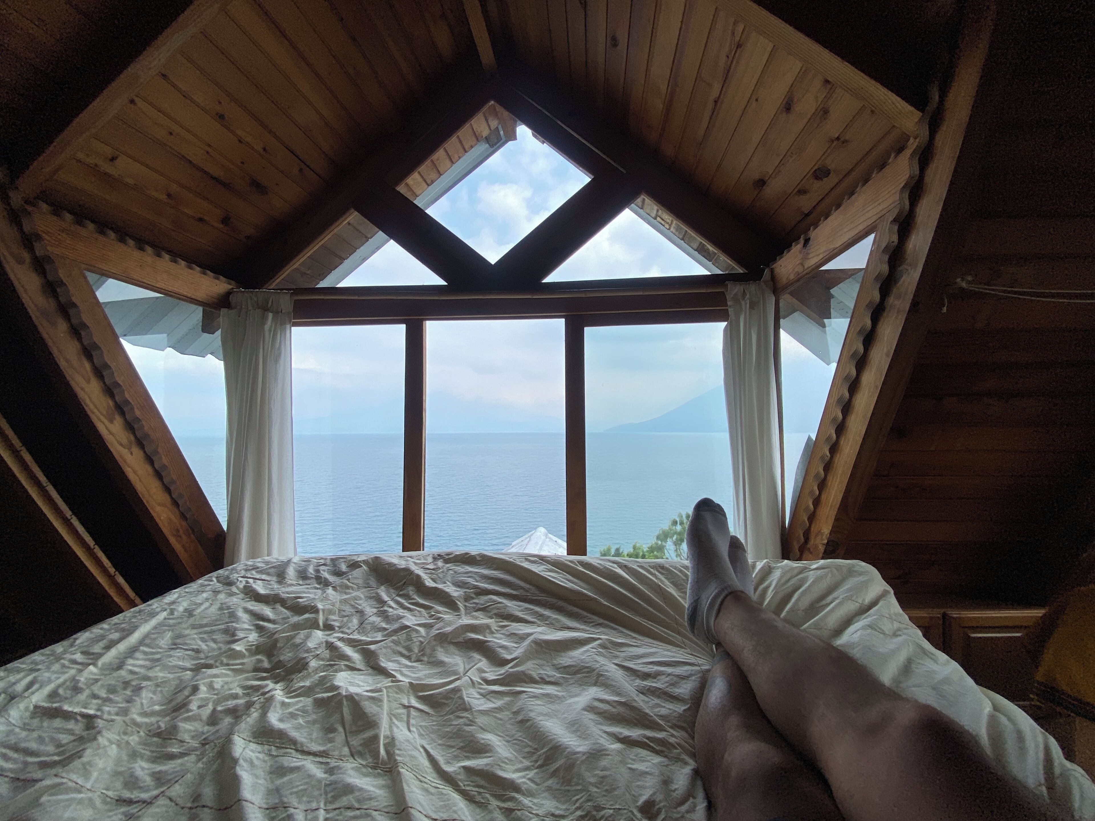Un dormitorio con una cama grande, vigas de madera en el techo y vista al mar a través de una ventana.