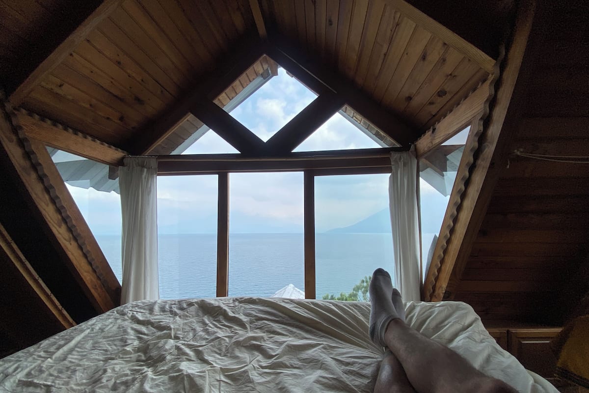 Een slaapkamer met een groot bed, houten balken in het plafond en uitzicht op zee door een raam.