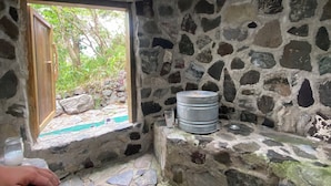 A rustic stone room with a window, a stone bench, and a metal container. - Blue Forest (San Marcos La Laguna)