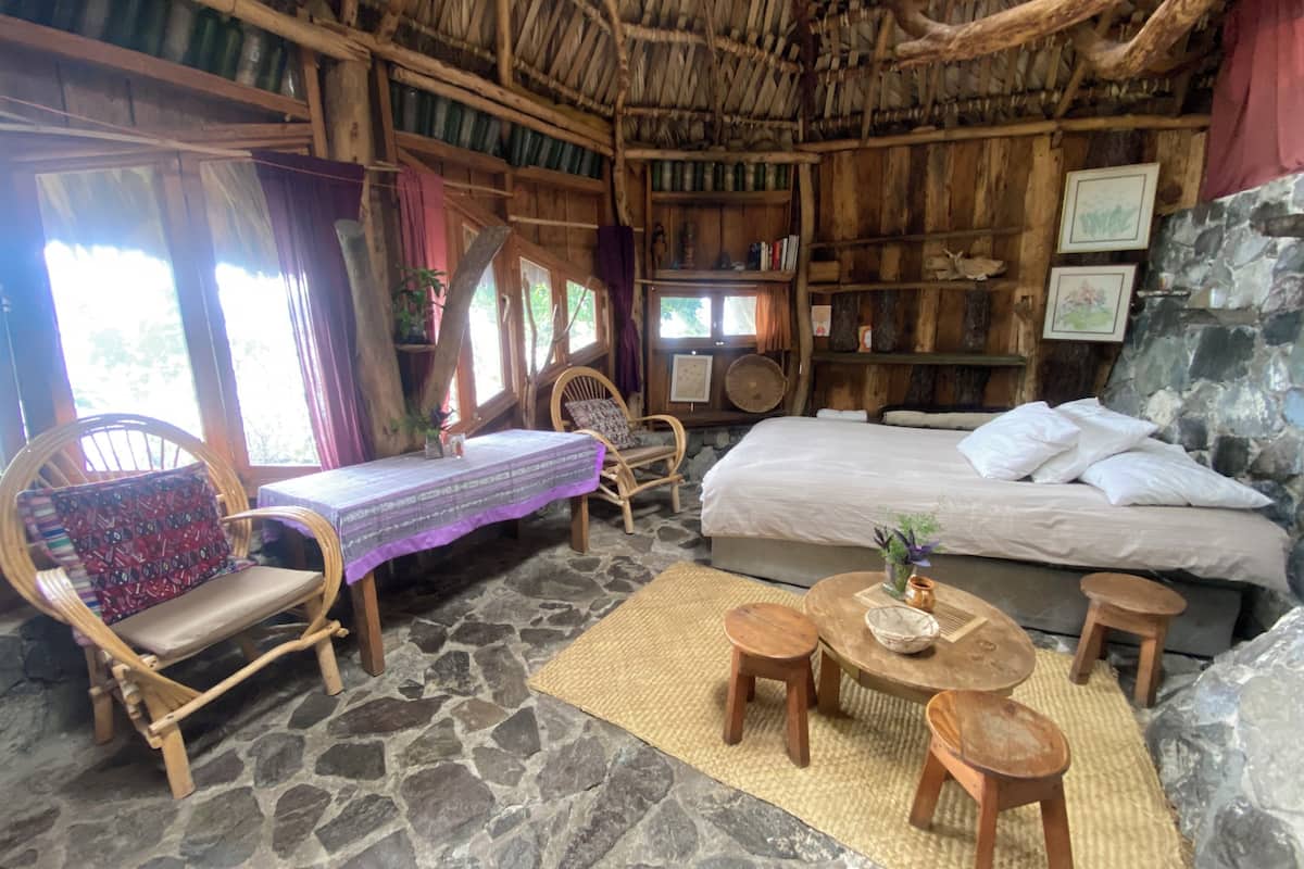 Een rustieke kamer met een stenen vloer, houten meubels, een bed en een rieten dak.