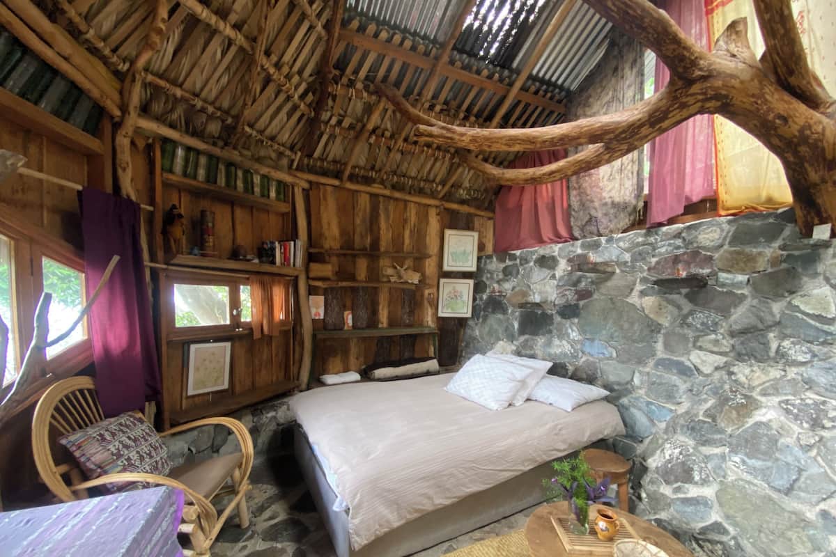 Een rustieke kamer met een bed, houten planken, een stenen muur en een geweven plafond.