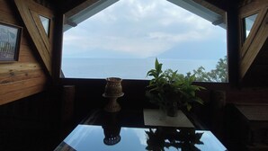 A room with a view of the sea through a triangular window, a table with a vase and a plant, and wooden walls. - Blue Forest (San Marcos La Laguna)