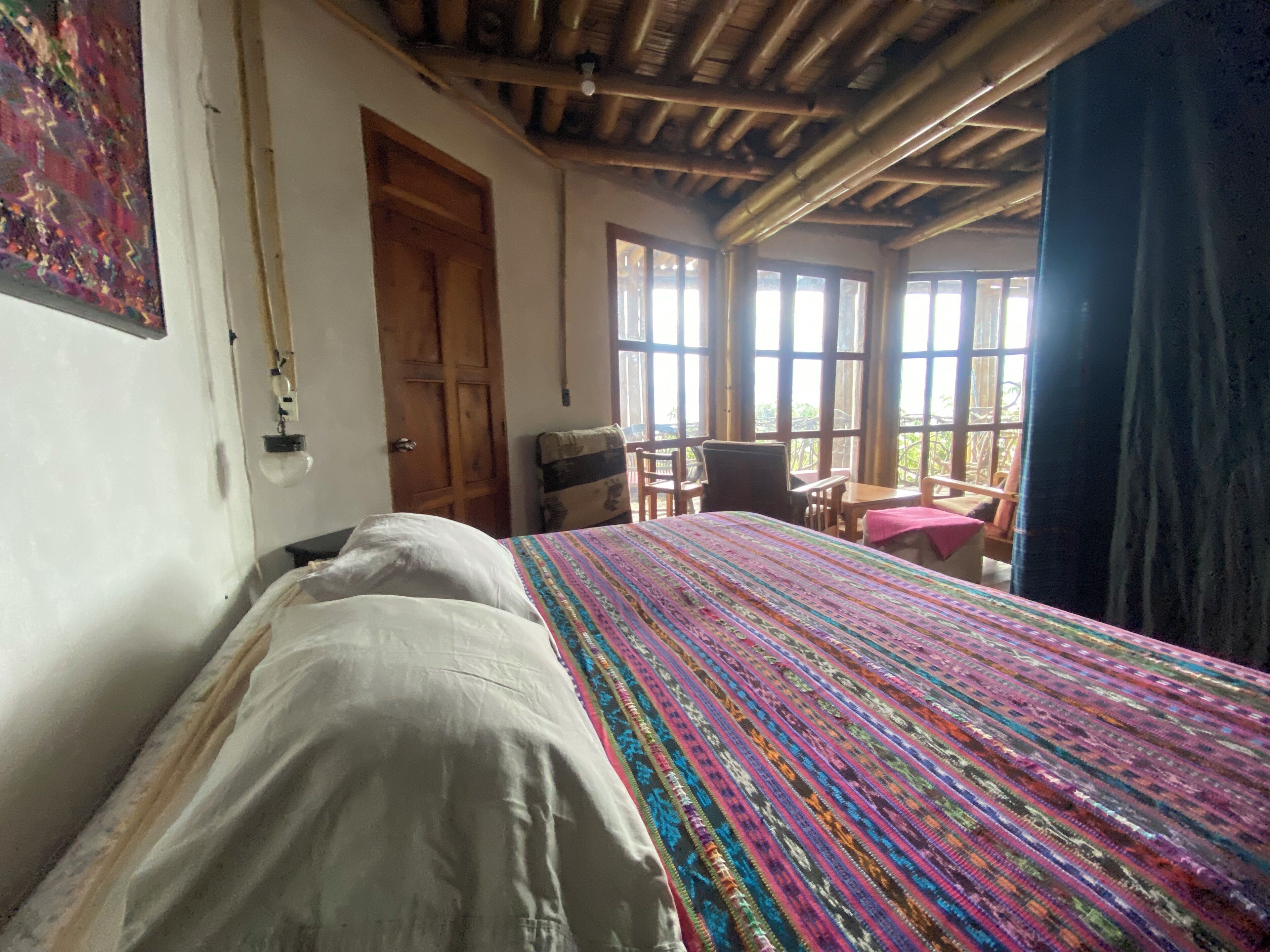 Una habitación con una cama, una puerta de madera, una ventana y vistas a la vegetación.