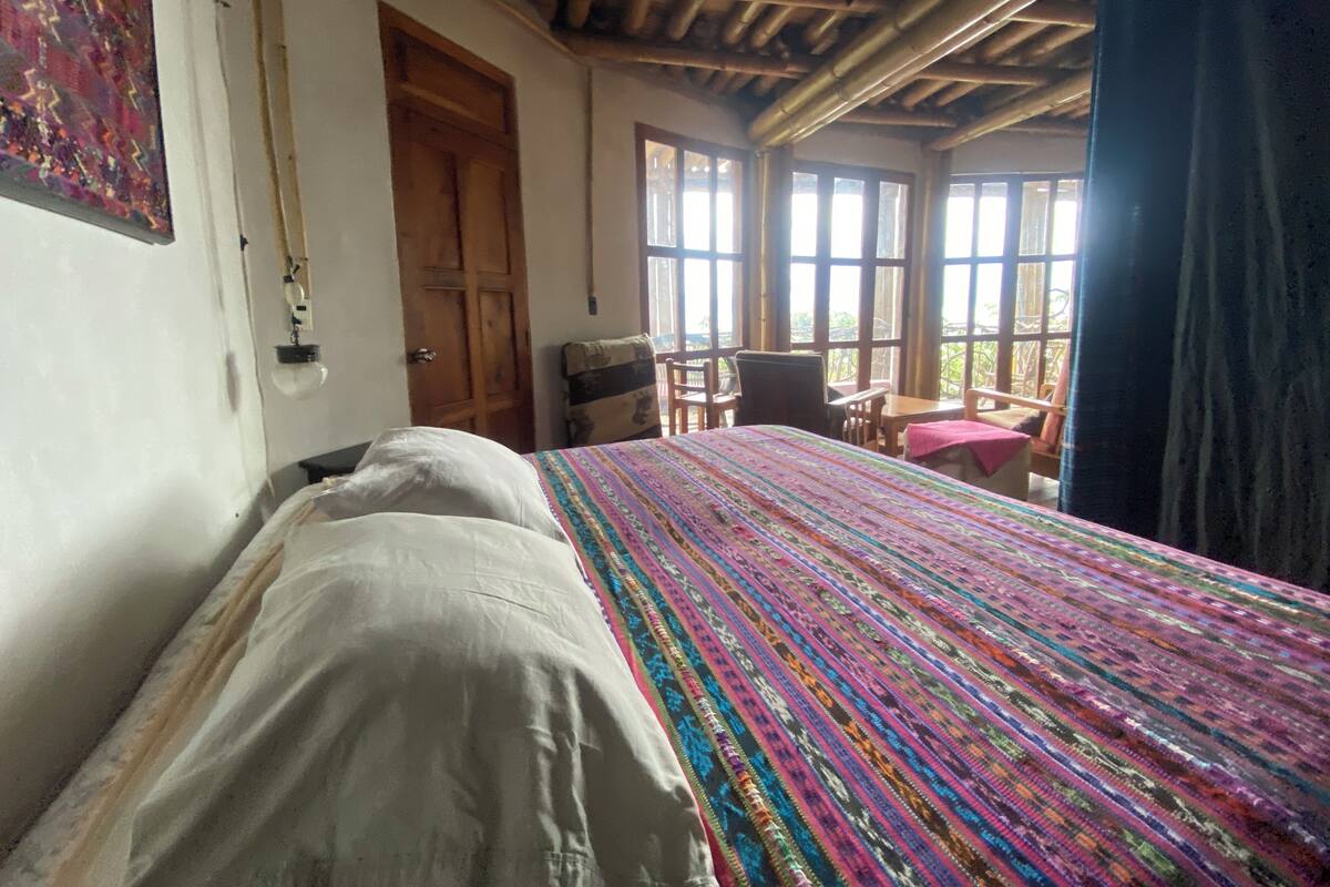 Een kamer met een bed, een houten deur, een raam en uitzicht op groen buiten.