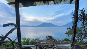 A wooden bench and table under a corrugated roof overlooking a calm lake with mountains in the distance. - Blue Forest (San Marcos La Laguna)