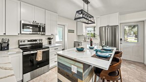 A modern kitchen with white cabinetry, stainless steel appliances, and a central island with blue bowls. - Low Tide – Pool, Pet Friendly, In SK Village - Walk Everywhere! (Siesta Key)