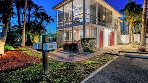 A modern two-story house with a balcony, surrounded by palm trees and a well-maintained garden. - Low Tide – Pool, Pet Friendly, In SK Village - Walk Everywhere! (Siesta Key)