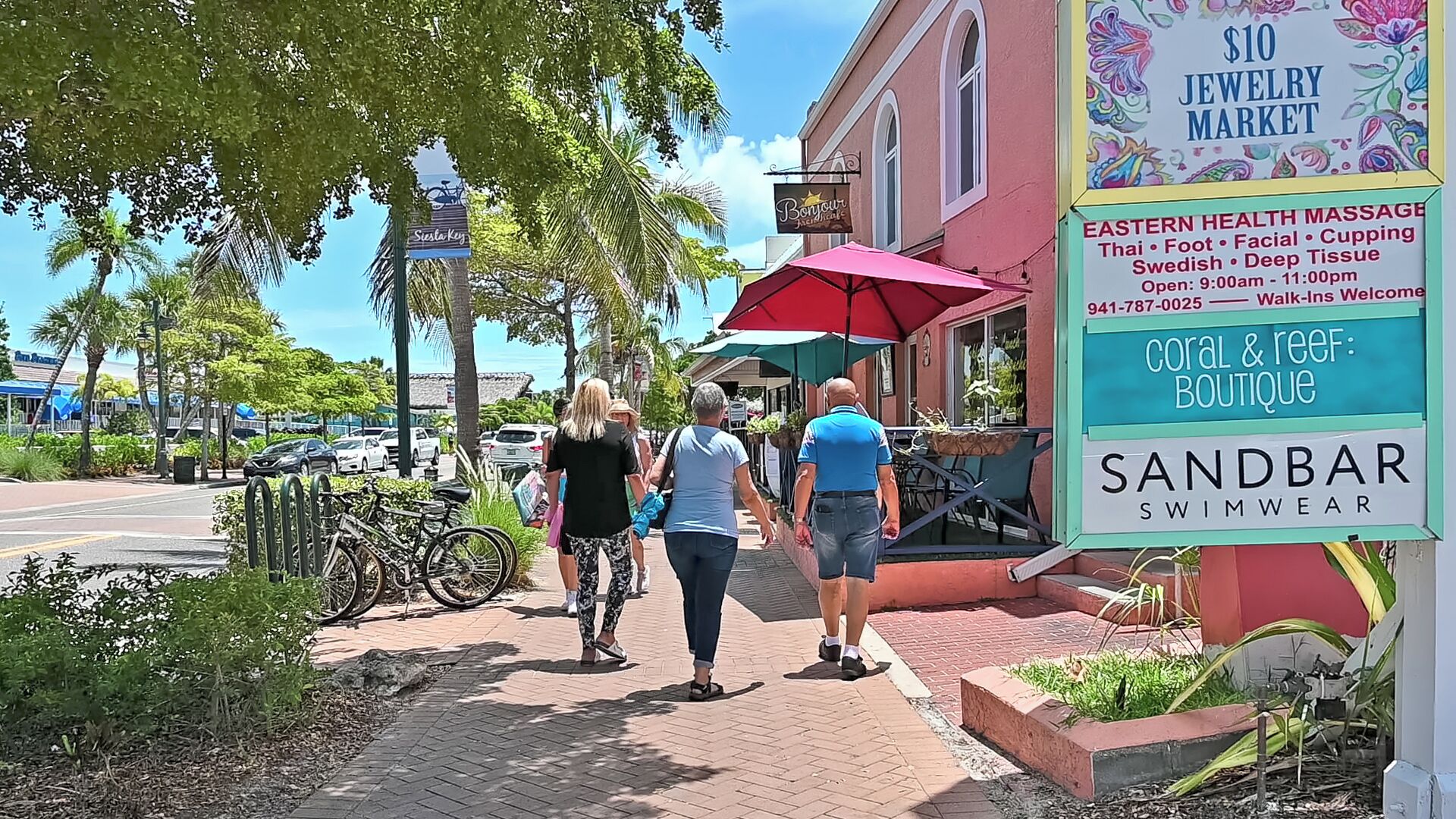 En trottoar med folk som promenerar, en skylt som visar vägen till en smyckesmarknad där priserna börjar på 10 dollar, och en skylt för Eastern Health Massage.