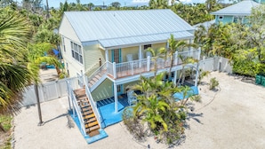 A two-story house with a balcony, a pool, and a sandy yard.