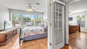 A bedroom with a bed, dresser, and a view of the outdoors through large windows.