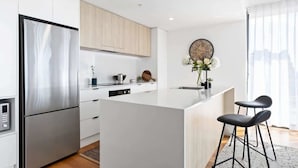 A modern kitchen with a stainless steel refrigerator, white cabinetry, a central island with bar stools, and a decorative clock on the wall.