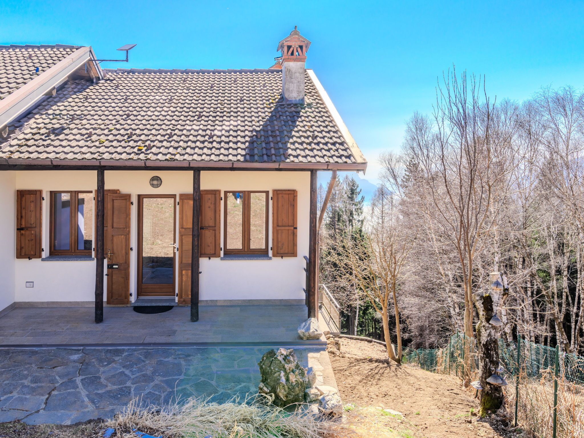 Un bâtiment à deux étages, doté d’un toit en tuiles, d’une piscine en pierre et d’une terrasse en bois.