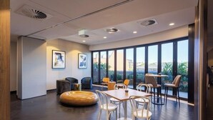 A modern hotel lobby with a large window, a round wooden bench, and a dining area with chairs and tables. - High-level 1 Bedroom Apartment in Fortitude Valley (Fortitude Valley)